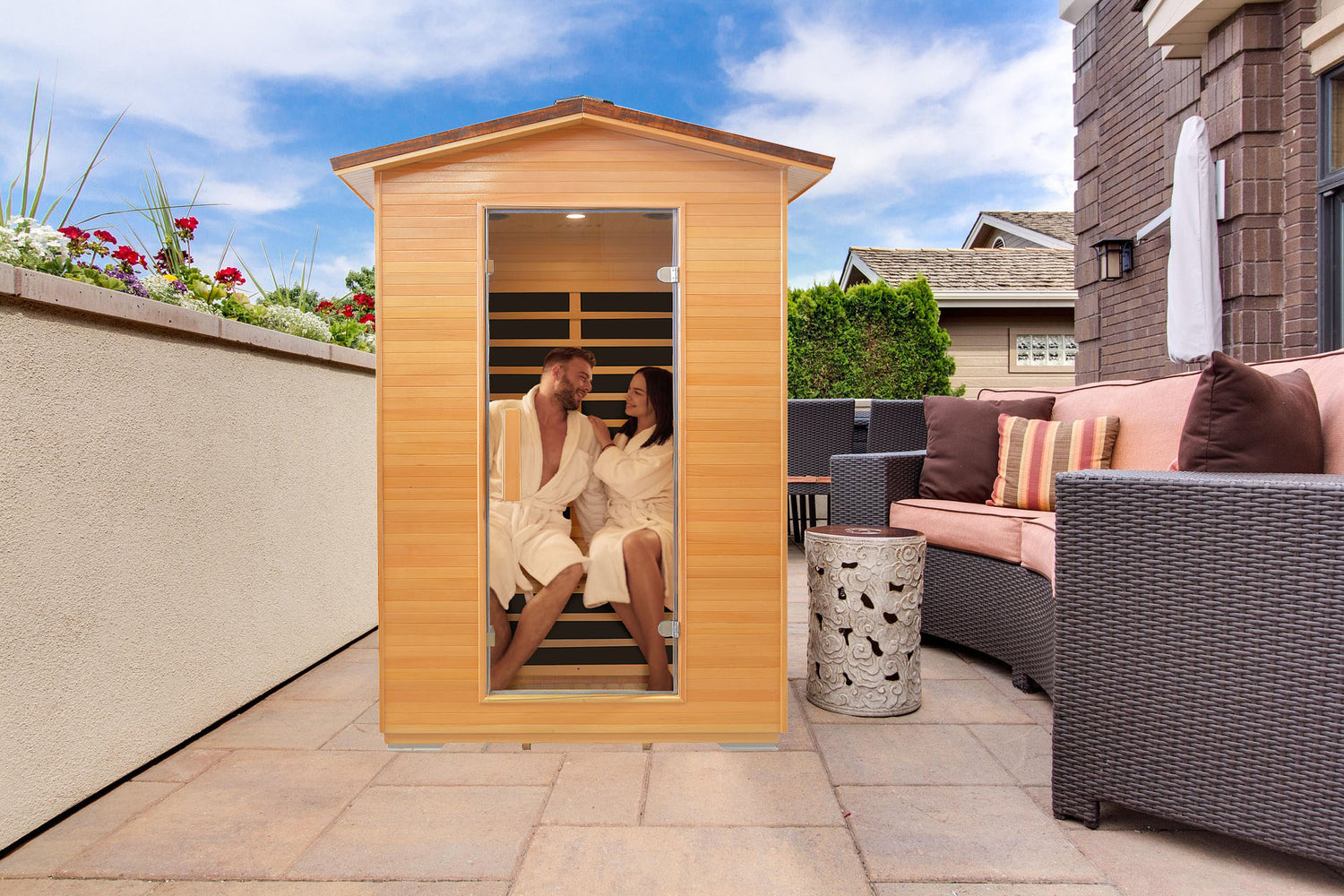 Two people in a wooden sauna on a patio with outdoor furniture and plants.