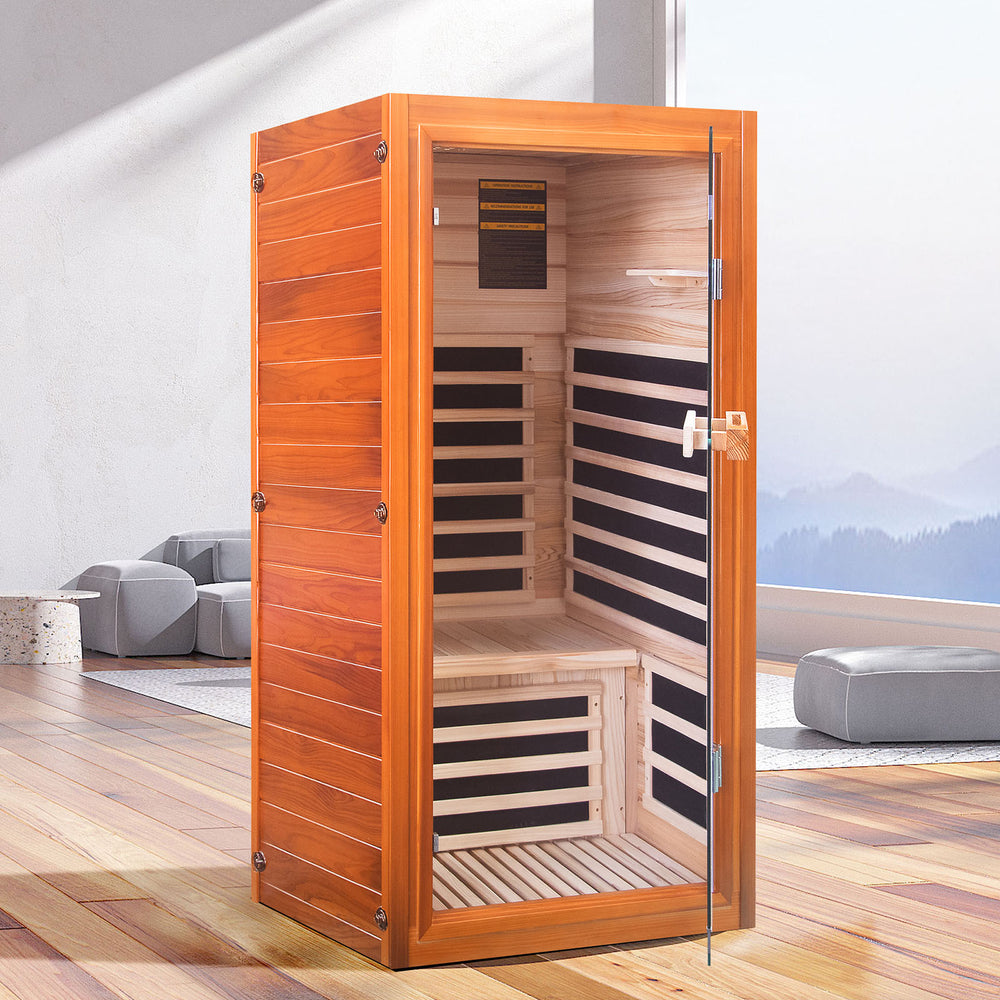 Wooden sauna with glass door in a room with gray sofa and wooden floor