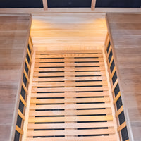 Wooden sauna bench with black rubber strips in a wooden room.