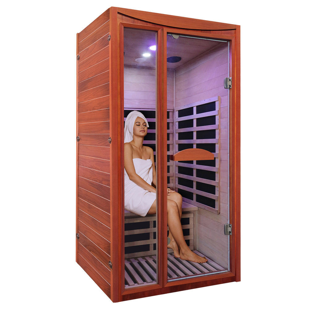 Person sitting inside a wooden infrared sauna with glass doors.